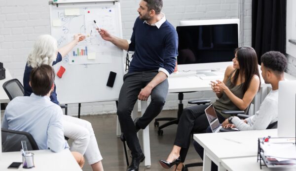 Creative people sitting at table in boardroom with man explaining business strategy