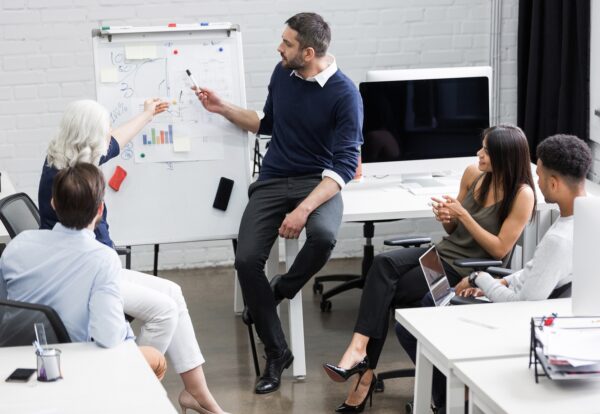 Creative people sitting at table in boardroom with man explaining business strategy