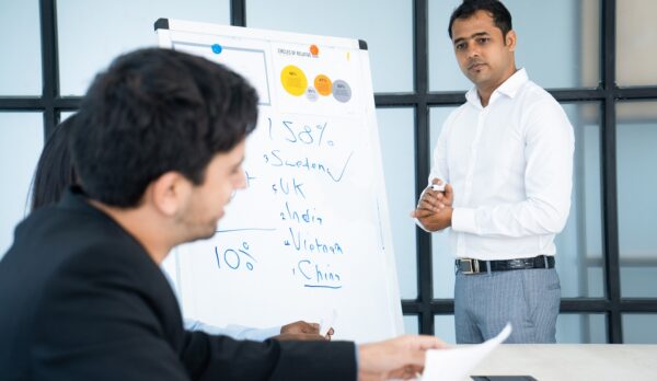 Pensive Indian business trainer listening to audience questions after presentation. Serious confident speaker working with audience and answering questions. Sales forecast concept